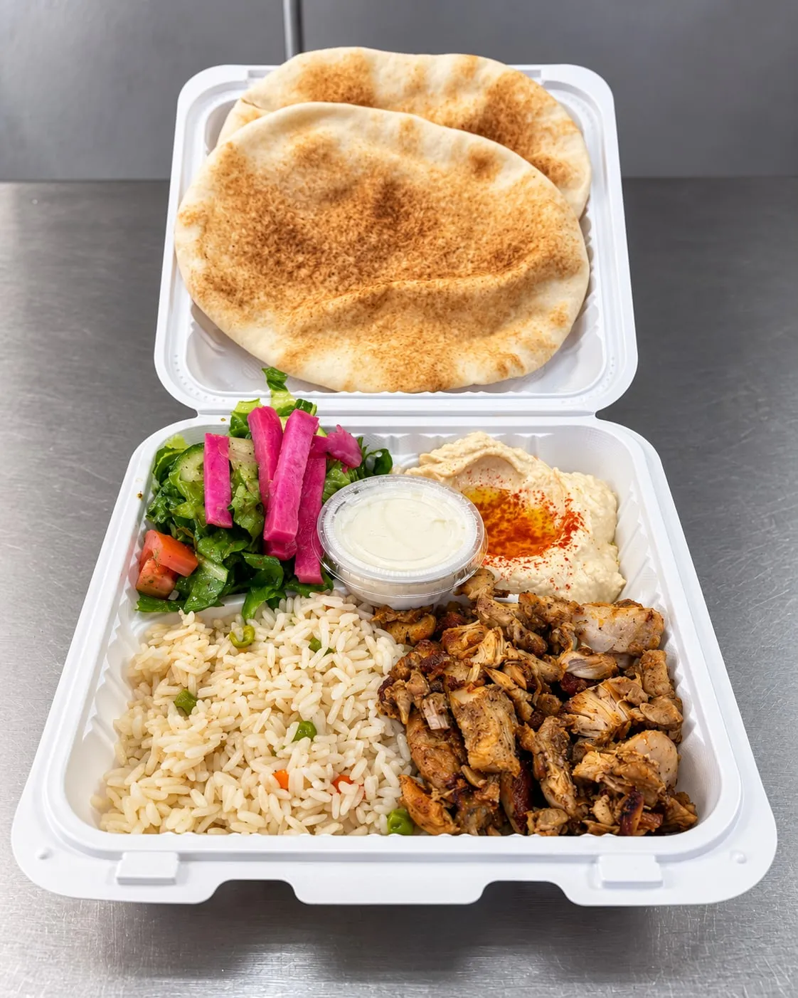 Chicken shawarma plate with rice, hummus, salad, pickled turnips, garlic sauce, and pita