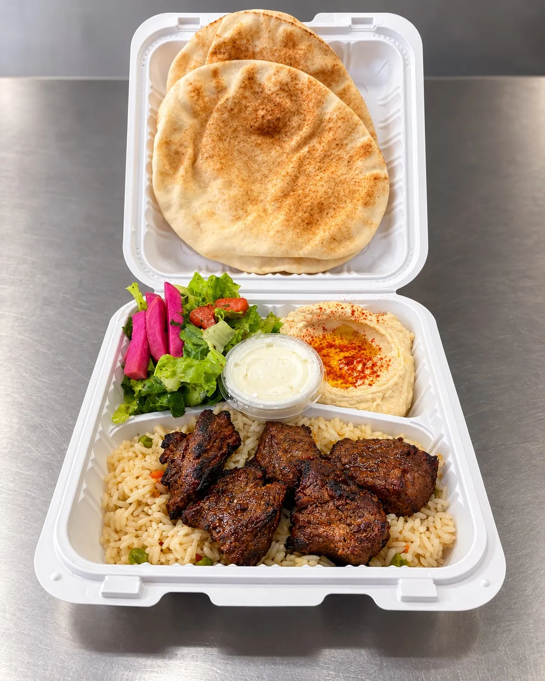 Grilled beef kabab plate with rice, hummus, salad, pickled turnips, garlic sauce, and pita
