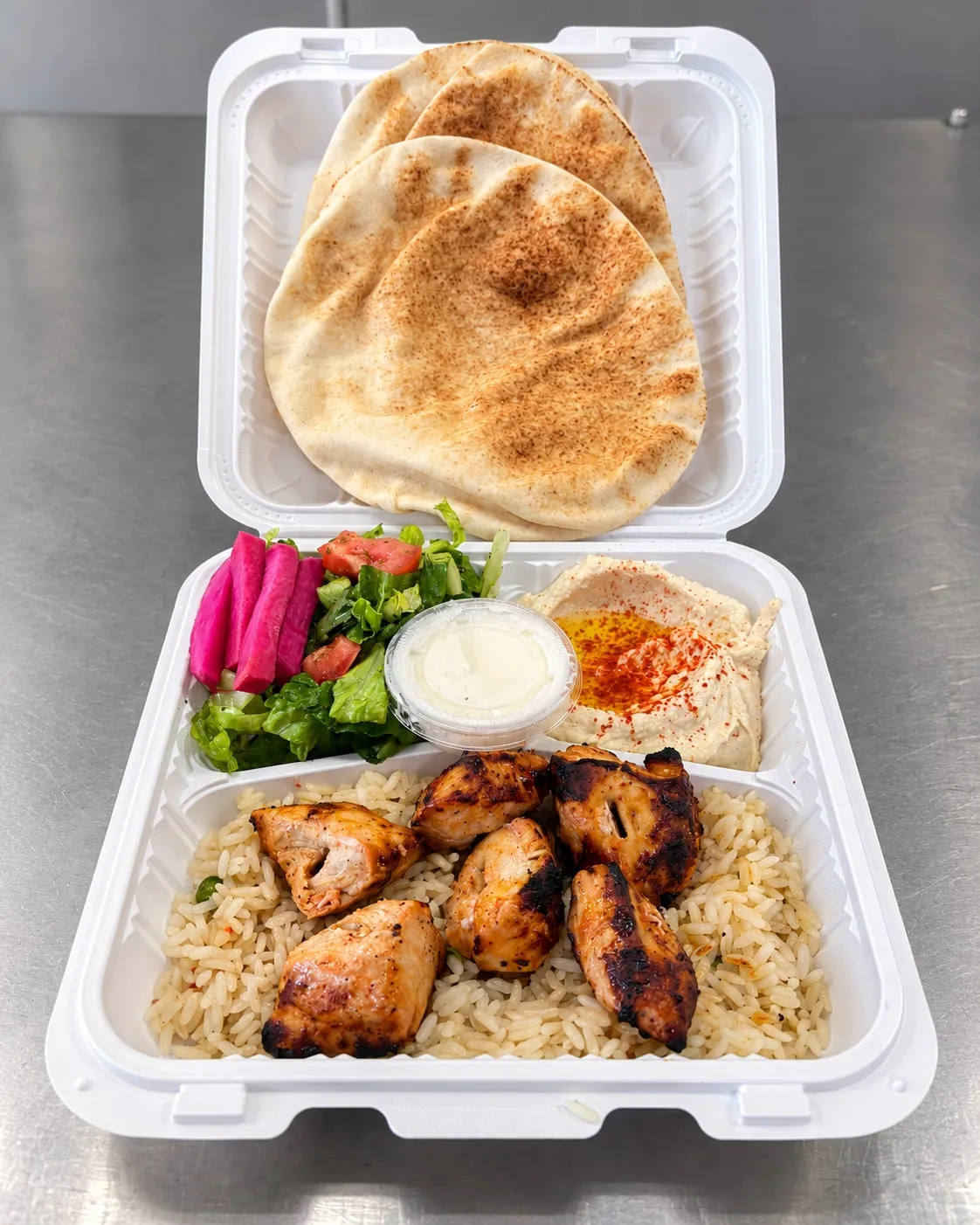 Grilled chicken kabab plate with rice, hummus, salad, pickled turnips, garlic sauce, and pita